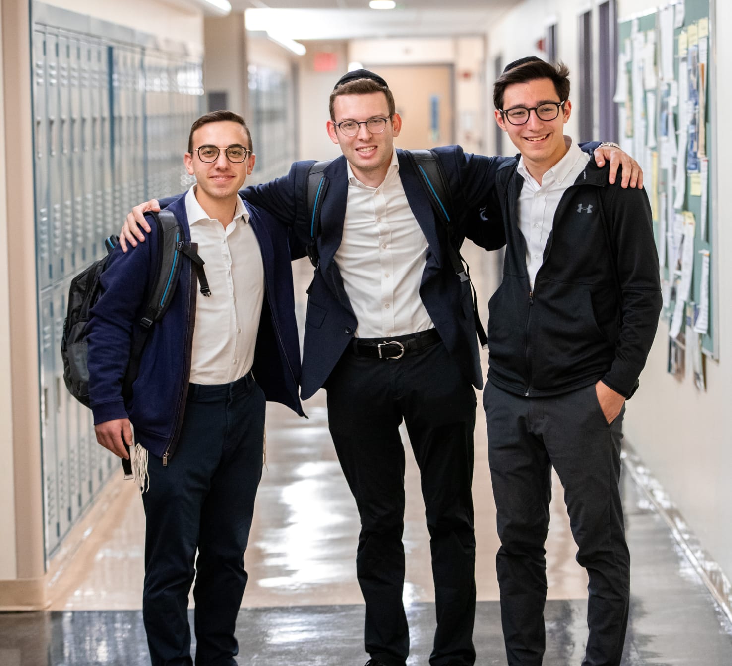 student with his arms around two other students in college hallway